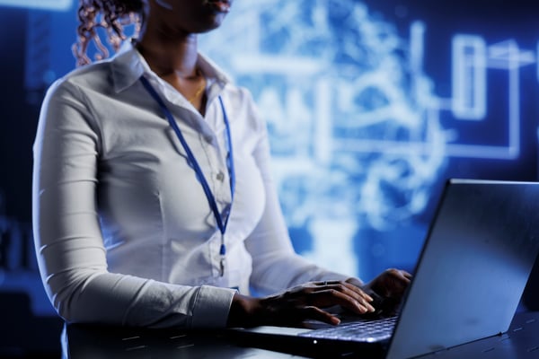 Cybersecurity professional typing on a laptop, with a digital brain and network diagram in the background, symbolizing tech and data protection.