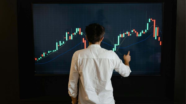 大型スクリーンの金融チャートを分析する人物。金融分析のための安全なデータ共有とマルチパーティ計算を象徴。