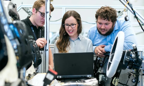 Team of engineers collaborating around a laptop in an automotive lab, working on advanced vehicle technology and innovation solutions.