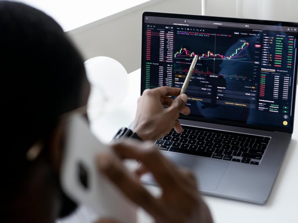 不審な取引をノートパソコンの画面上でローソク足チャートを使って分析し、金融詐欺や不規則な取引に気づく可能性のある人物。
