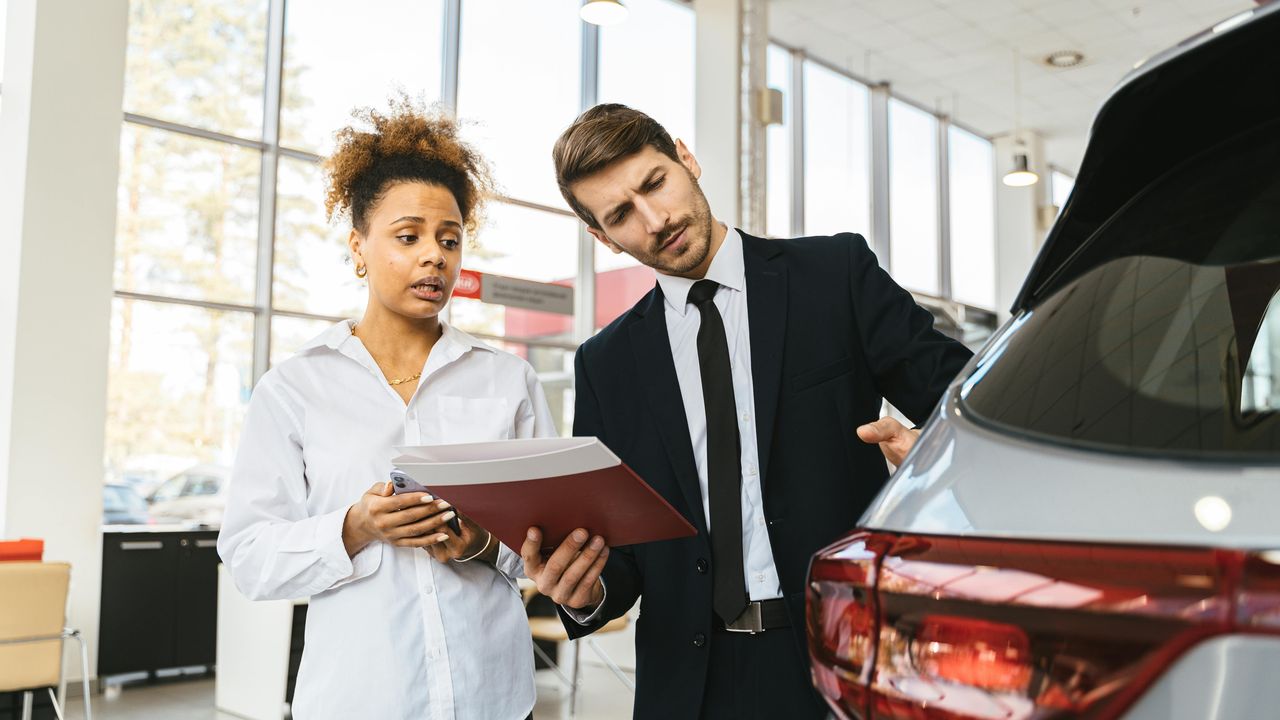 Two professionals discussing documents beside a car, representing data-driven solutions and innovation for the automotive industry.
