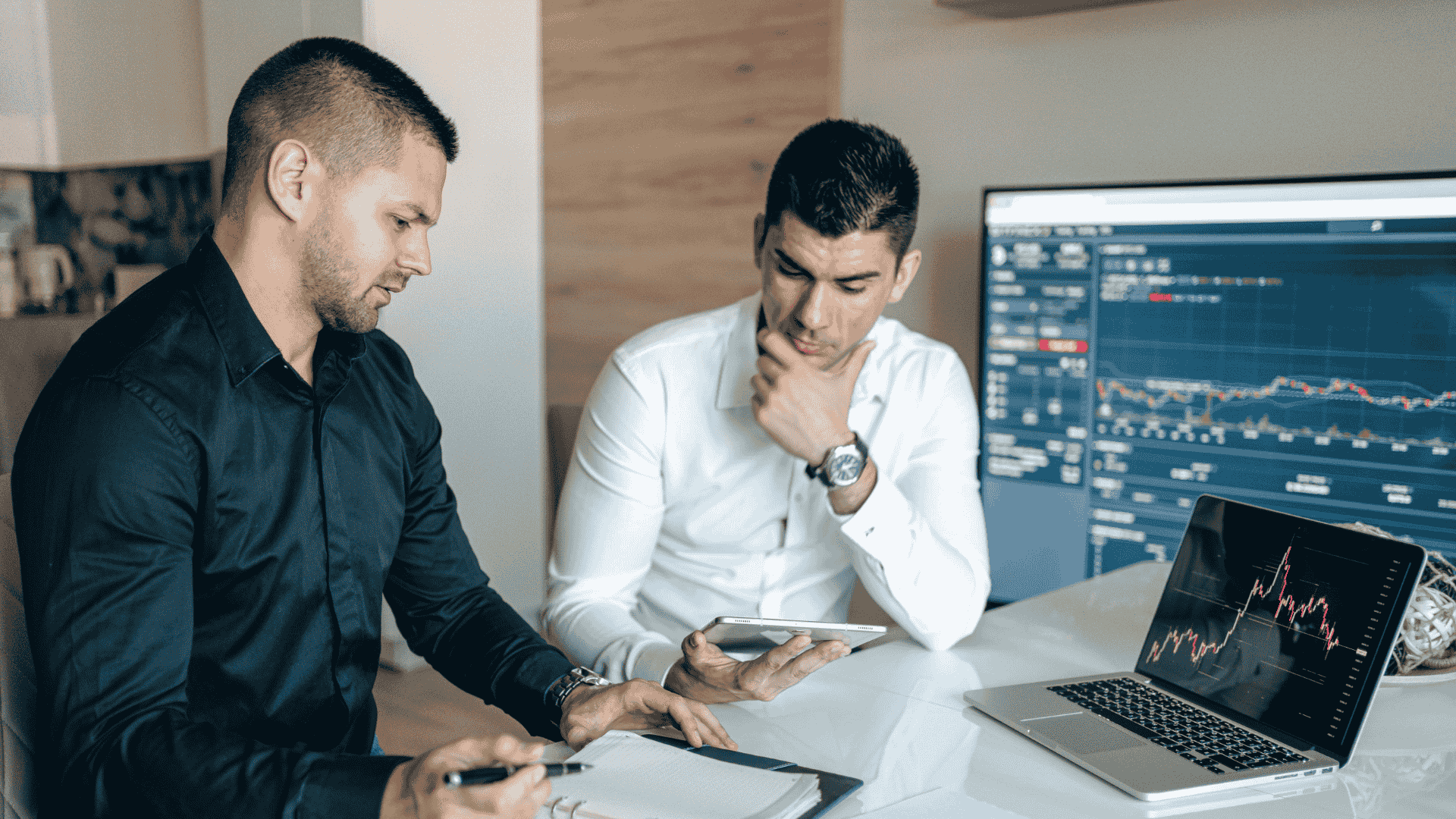 Two professionals analyzing financial data on screens and devices, representing AML compliance, UK financial crime prevention, and regulatory reporting.