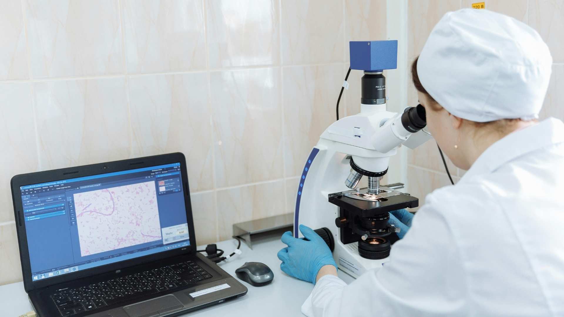 Lab technician analyzing samples with a microscope connected to a laptop, demonstrating the use of health tech in medical diagnostics.